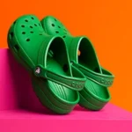 a pair of green crocs sandals on a pink surface